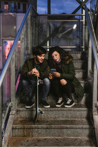Couple of teenagers look at the smartphone on an outdoors staircase