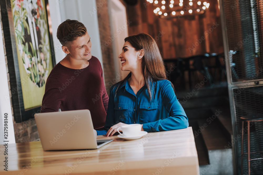 Concept of successful team work. Waist up portrait of young cheerful man and woman working on laptop in cozy cafe Concept of successful team work. Waist up portrait of young cheerful man and woman working on laptop in cozy cafe