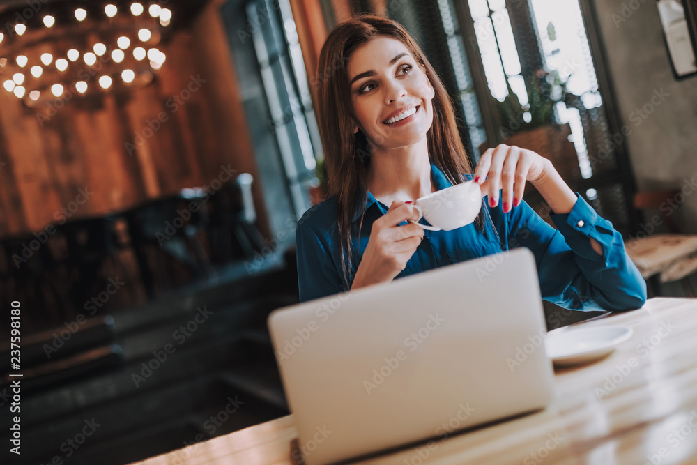 Concept of success and freelance work. Waist up portrait of smiling business lady drinking coffee while working on notebook in cozy cafe Concept of success and freelance work. Waist up portrait of smiling business lady drinking coffee while working on notebook in cozy cafe