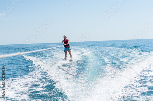 Young man glides on water skiing on the waves on the sea, ocean. Healthy lifestyle. Positive human emotions, joy. Family are spending time at tropical ocean in the day time. New Zealand.