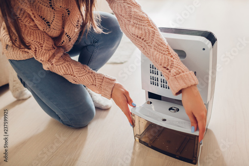 Woman changing water container of dehumidifier at home. Dampness in apartment. Modern air dryer photo