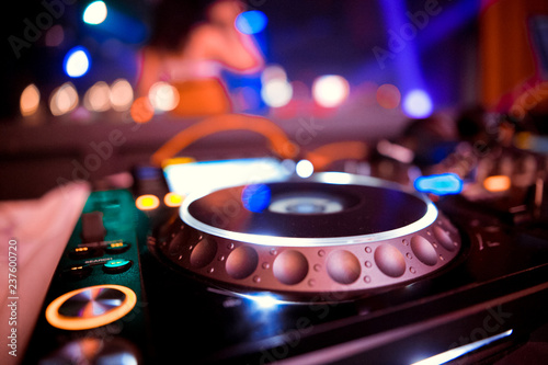 Close up view of the hands of a male disc jockey mixing music on his deck with his hands poised over the vinyl record on the turntable and the control switches at night