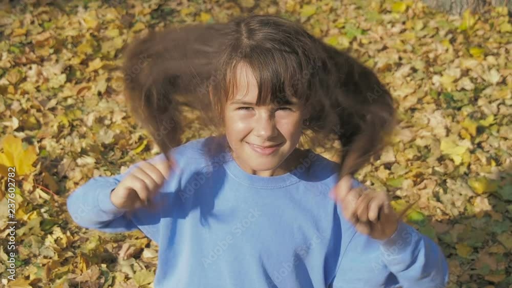 Portrait of a happy child. Cheerful little girl is playing with her hair in autumn in the park. Portrait of a happy child. Cheerful little girl is playing with her hair in autumn in the park.