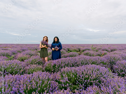 Two young girls with different hair color in blue and green dresses, posing together in a lavender field.