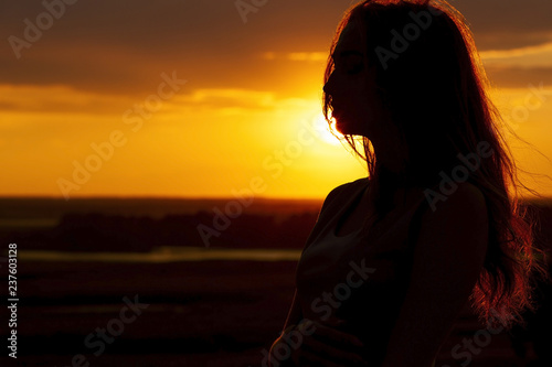 silhouette of a beautiful romantic girl at sunset , face profile of young woman with long hair in hot weather