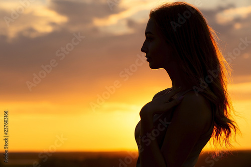 silhouette of a beautiful romantic girl at sunset , face profile of young woman with long hair in hot weather