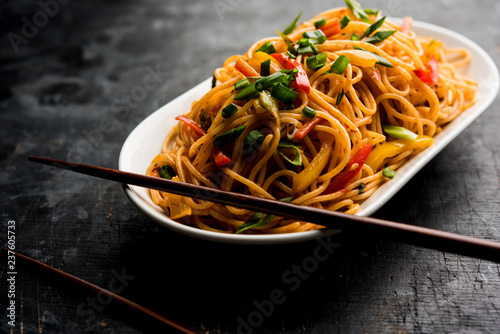 Schezwan Noodles or vegetable Hakka Noodles or chow mein is a popular Indo-Chinese recipes, served in a bowl or plate with wooden chopsticks. selective focus