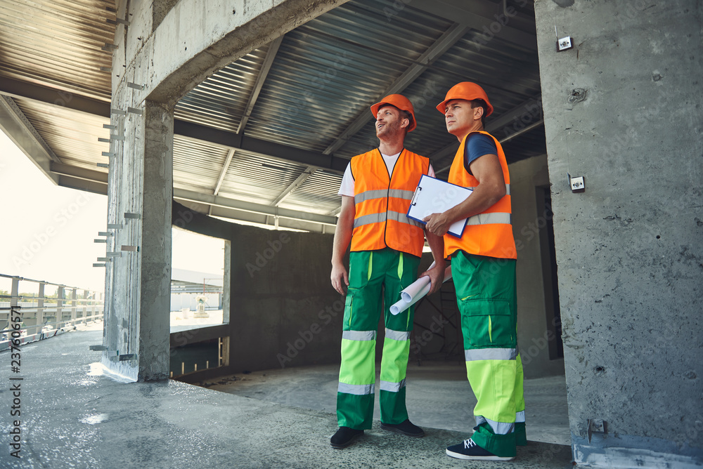 Confident professional builders looking at the results of their work and feeling satisfied Confident professional builders looking at the results of their work and feeling satisfied