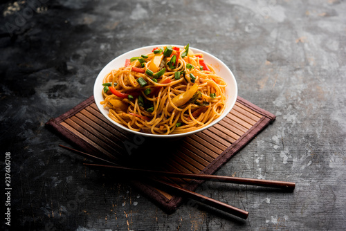 Schezwan Noodles or vegetable Hakka Noodles or chow mein is a popular Indo-Chinese recipes, served in a bowl or plate with wooden chopsticks. selective focus