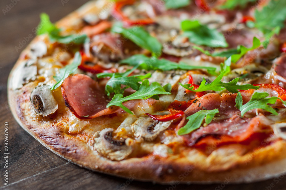 Pizza with Mozzarella cheese, mushrooms, ham, tomato sauce, salami, pepper, Spices and Fresh arugula. Italian pizza on wooden table background Pizza with Mozzarella cheese, mushrooms, ham, tomato sauce, salami, pepper, Spices and Fresh arugula. Italian pizza on wooden table background