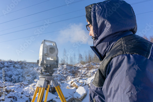 A surveyor conducts a topographical survey for the cadastre at a construction site in winter