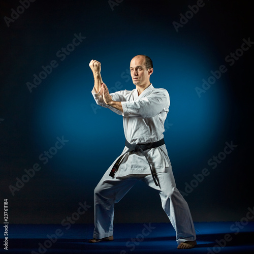On blue tatami adult athlete trains formal exercises karate