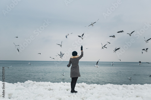 Girl feeding seagulls on the frozen bank of the winter sea