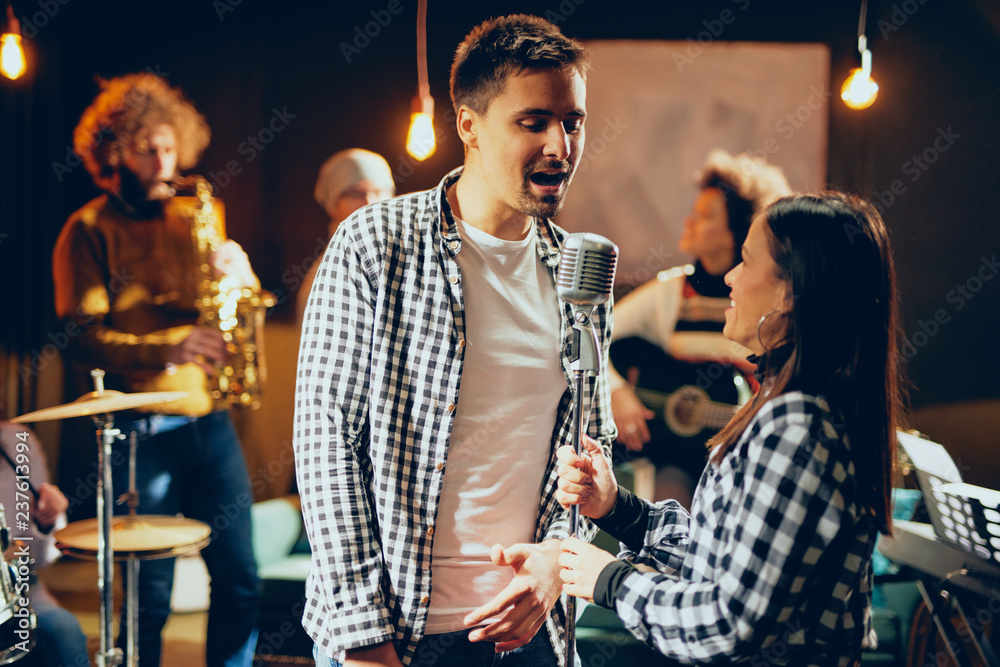Fototapeta premium Singers practicing for duet. In background band playing. Home studio interior.