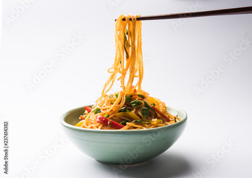 Schezwan Noodles or vegetable Hakka Noodles or chow mein is a popular Indo-Chinese recipes, served in a bowl or plate with wooden chopsticks. selective focus photo
