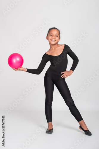 Studio shot of attractive little gymnast girl of wearing black leggings and  a bathing suit with a green jump rope on a white background, full length.  Stock Photo