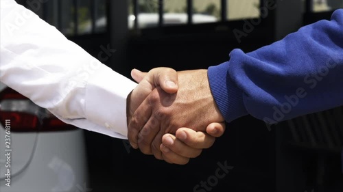 Two men confirm car sale or hire deal by shaking hands next to brand new shiny white car