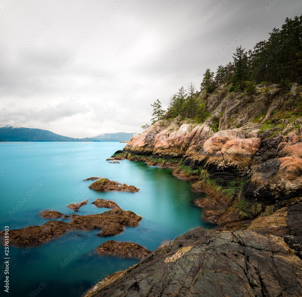 Beautiful blue bay water contrasts with orange cliffs and a grey overcast sky
