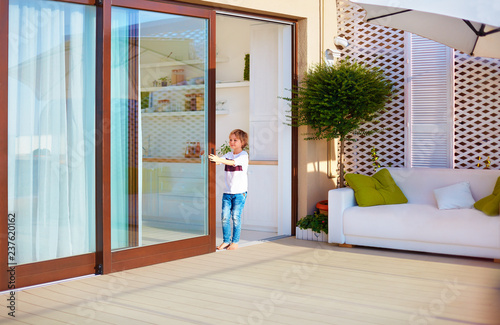 happy young boy, kid opening the sliding door on rooftop patio area at home
