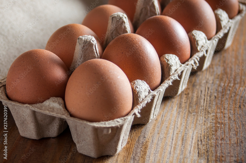 Large brown chicken eggs in green carton packaging on wooden table. Large brown chicken eggs in green carton packaging on wooden table.