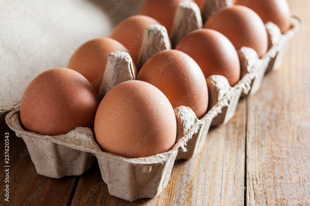 Large brown chicken eggs in green carton box on wooden table. Large brown chicken eggs in green carton box on wooden table.