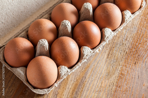 Brown chicken eggs in carton on wooden table.
