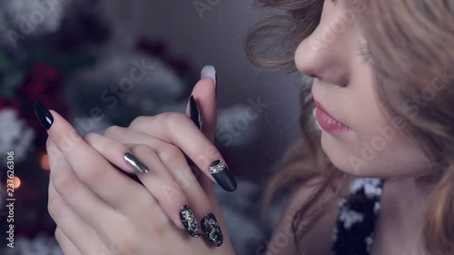 Beautiful smiling woman. Manicure nails. Makeup. Healthy long hair style. Elegant lady queen in black dress over christmas tree lights background.