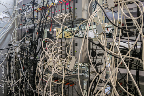 Many TV wires randomly intermingle among themselves in the racks of the server room of the TV station. Telecommunication equipment of a cable television provider