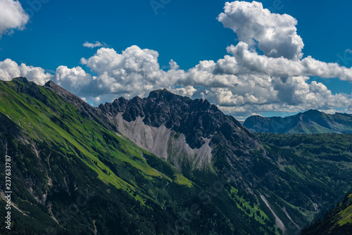 Felswände und grüne Flächen und Berggipfel mit blauem Himmel und einigen Wolken