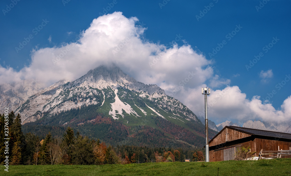 Alpine landscape on a sunny day. Colorful autumn scene. Mountain and a huge cloud above it. In the foreground is a relay tower and an alpine shed. Amazing natural background. South Tyrol Austria