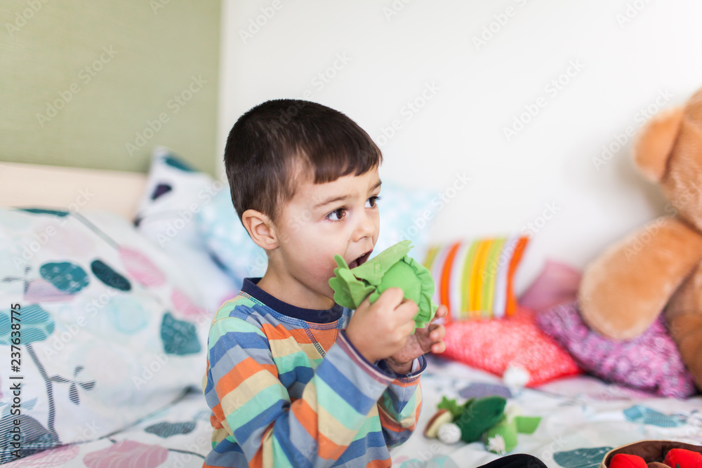 cute little boy is playing with colorful soft vegetables sitting on bed.