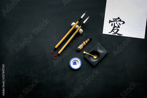 Chinese or japanese calligraphy concept. Hieroglyph love near traditional written accessories on black background top view space for text