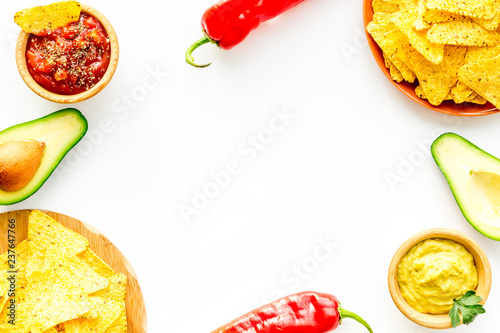 Popular mexican snack nachos. Tiangle nacho tortilla near salsa and guacamole sause, chili pepper, salt on white background top view copy space photo