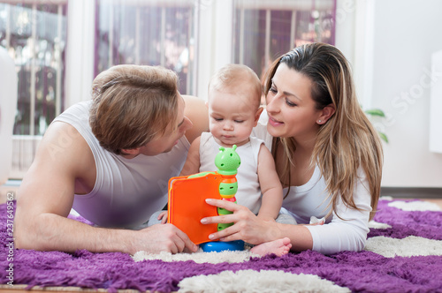 Happy parents laying down on the floor and playing with their baby boy.