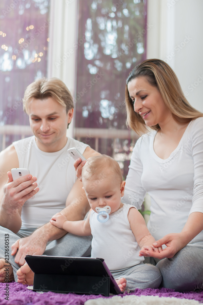 Obraz premium Happy parents sitting on the floor and playing with their baby boy. Computer era.