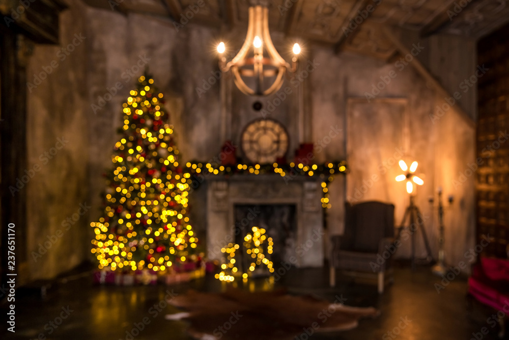 Defocused blurred background of dark room with christmas interior, Xmas Tree decorated with flashing garland. Darken decor with artificial fireplace