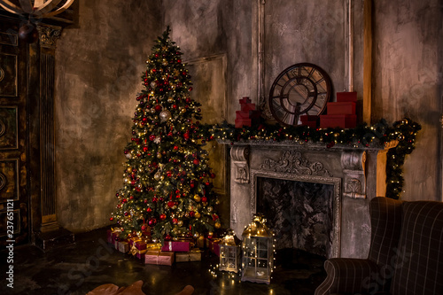 Dark room with christmas interior, Xmas Tree decorated with flashing garland. Darken decor with artificial fireplace