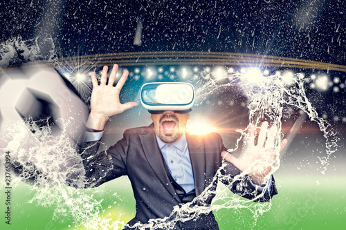 Business man with virtual reality glasses in a stadium with rain and a ball. Mixed Media