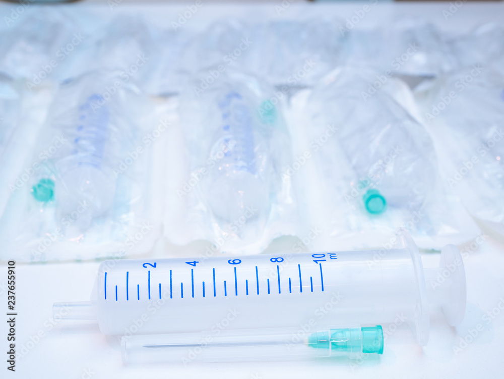 close-up of one unpacked medical syringe lay horizontally with needle unattached and lot of syringes packed on background out of focus, blurred close-up of one unpacked medical syringe lay horizontally with needle unattached and lot of syringes packed on background out of focus, blurred