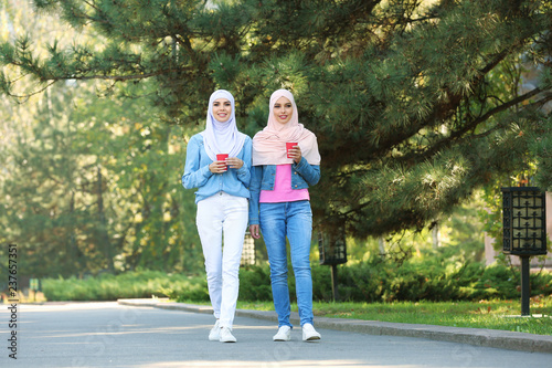 Muslim women with cups of coffee walking in park