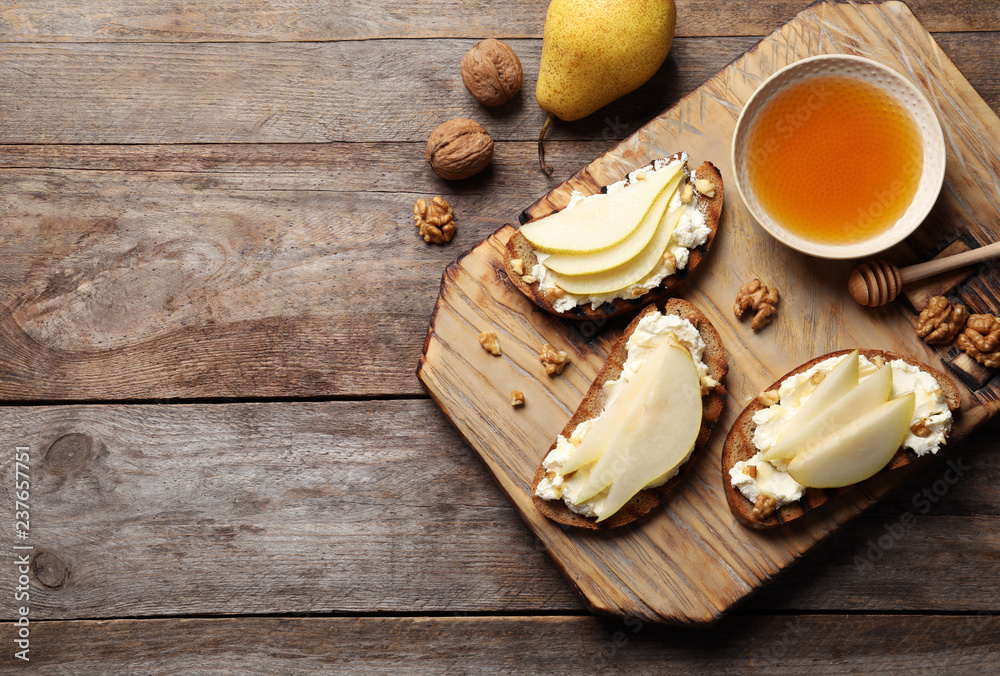 Toasted bread with tasty cream cheese and pear on wooden table, flat lay. Space for text