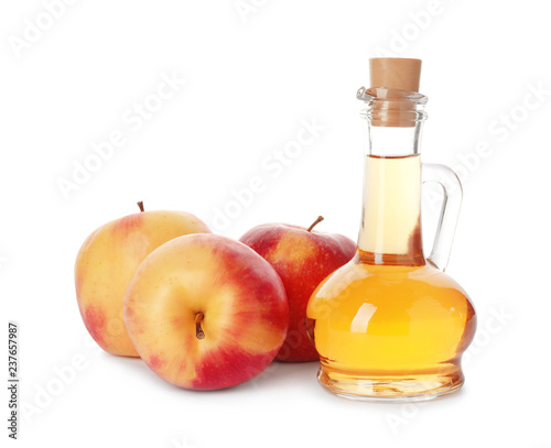 Glass jug of vinegar and fresh apples on white background