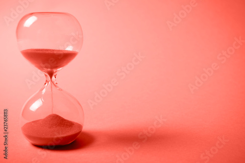 Hourglass with orange sand on gradient coral background. photo