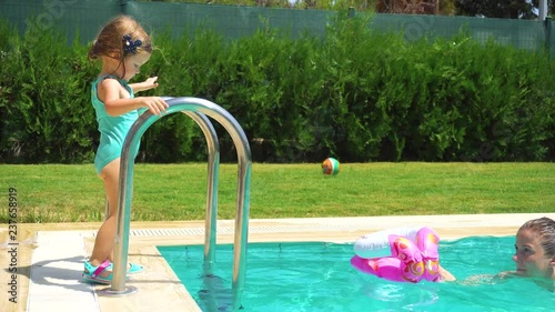 Mother and daughter helping to girl to enter in the pool