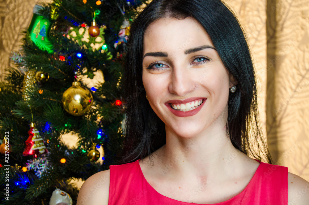 portrait of attractive caucasian smiling woman black hair on studio shot. caucasian girl with blue eyes near christmas tree. portrait of attractive caucasian smiling woman black hair on studio shot. caucasian girl with blue eyes near christmas tree.