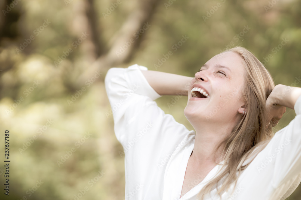 Euphoric woman smiling and laughing with her hands raised outdoors in nature
