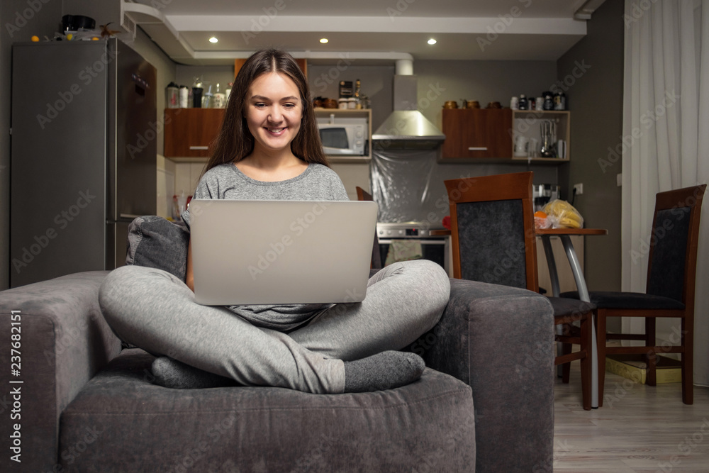 young woman communicates in social networks with laptop, girl sitting at home in chair with laptop young woman communicates in social networks with laptop, girl sitting at home in chair with laptop