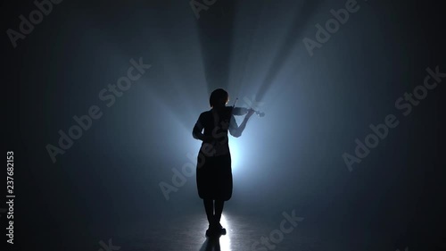 Girl plays the violin a classic composition in a dark smoky room. Silhouette. Black smoke background