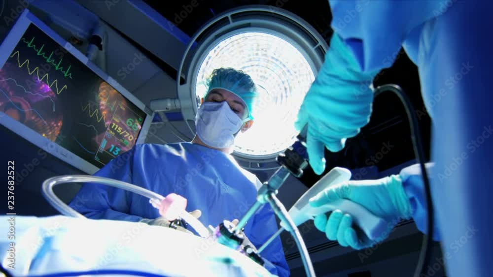 Medical Caucasian surgical team in scrubs performing Laparoscopy surgery on the patient in operating theatre using video camera technology 