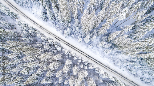Aerial viwe of road cutting through snow covered forest. Idyllic winter scenery
